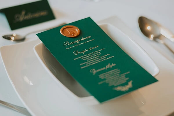 Zielona karta na z daniami i propozycja kolacji dla wszystkich gosci, położonona na stole z białym obrusem oraz zastawą podczas kolacji w restauracji obok Poznania